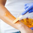 Women hold orange paraffin wax bowl. Woman in beauty salon.